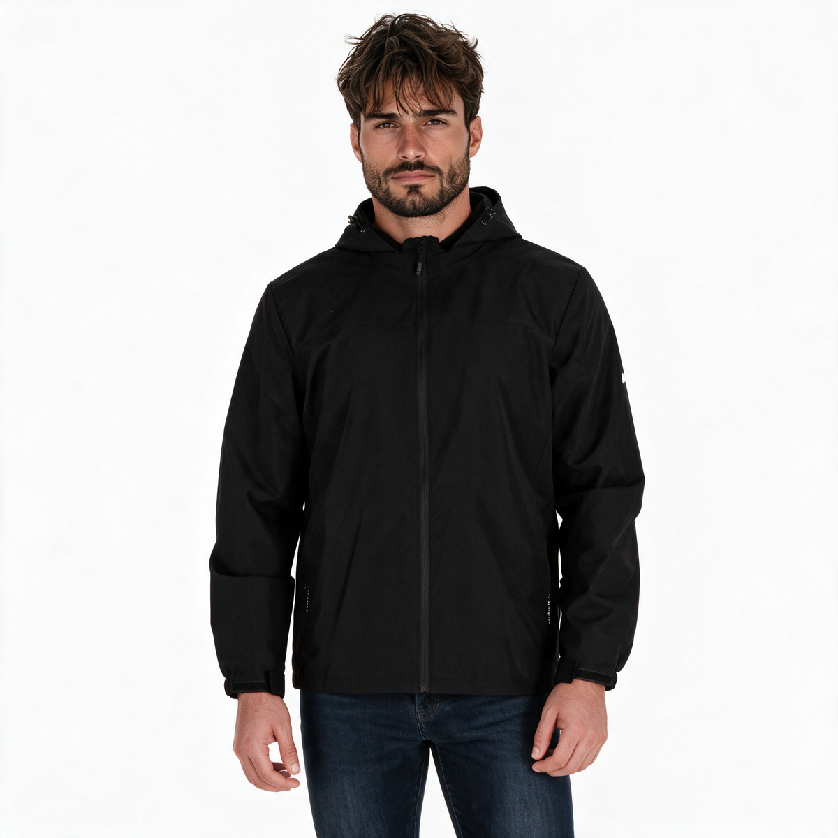 Hombre modelando chamarra TUUM Peak negra con capucha, cierre frontal y logotipo blanco en manga, combinada con pantalón beige sobre fondo blanco.