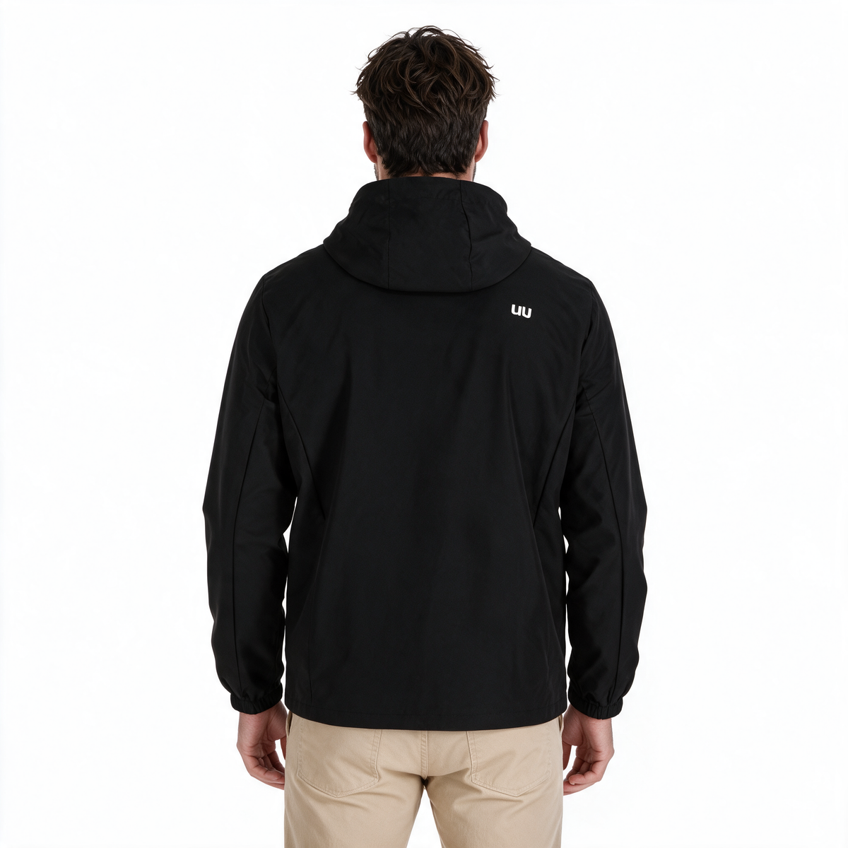 Hombre modelando chamarra TUUM Peak negra con capucha, cierre frontal y logotipo blanco en manga, combinada con pantalón beige sobre fondo blanco.